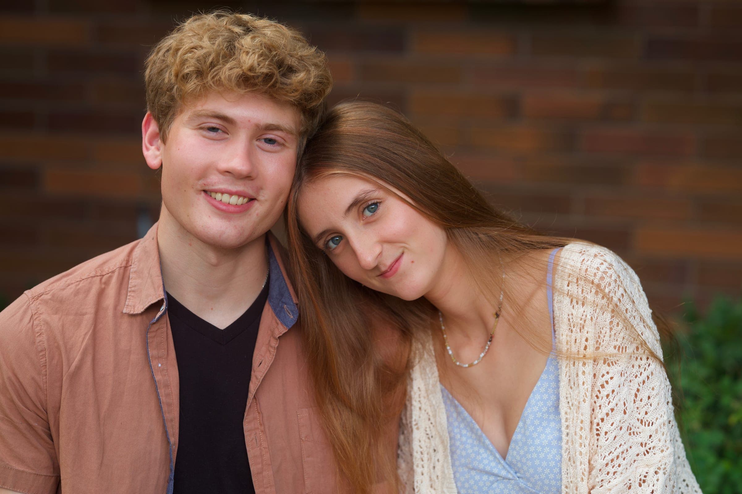 Molly resting her head on Tyler's shoulder in front of a brick wall, both smiling