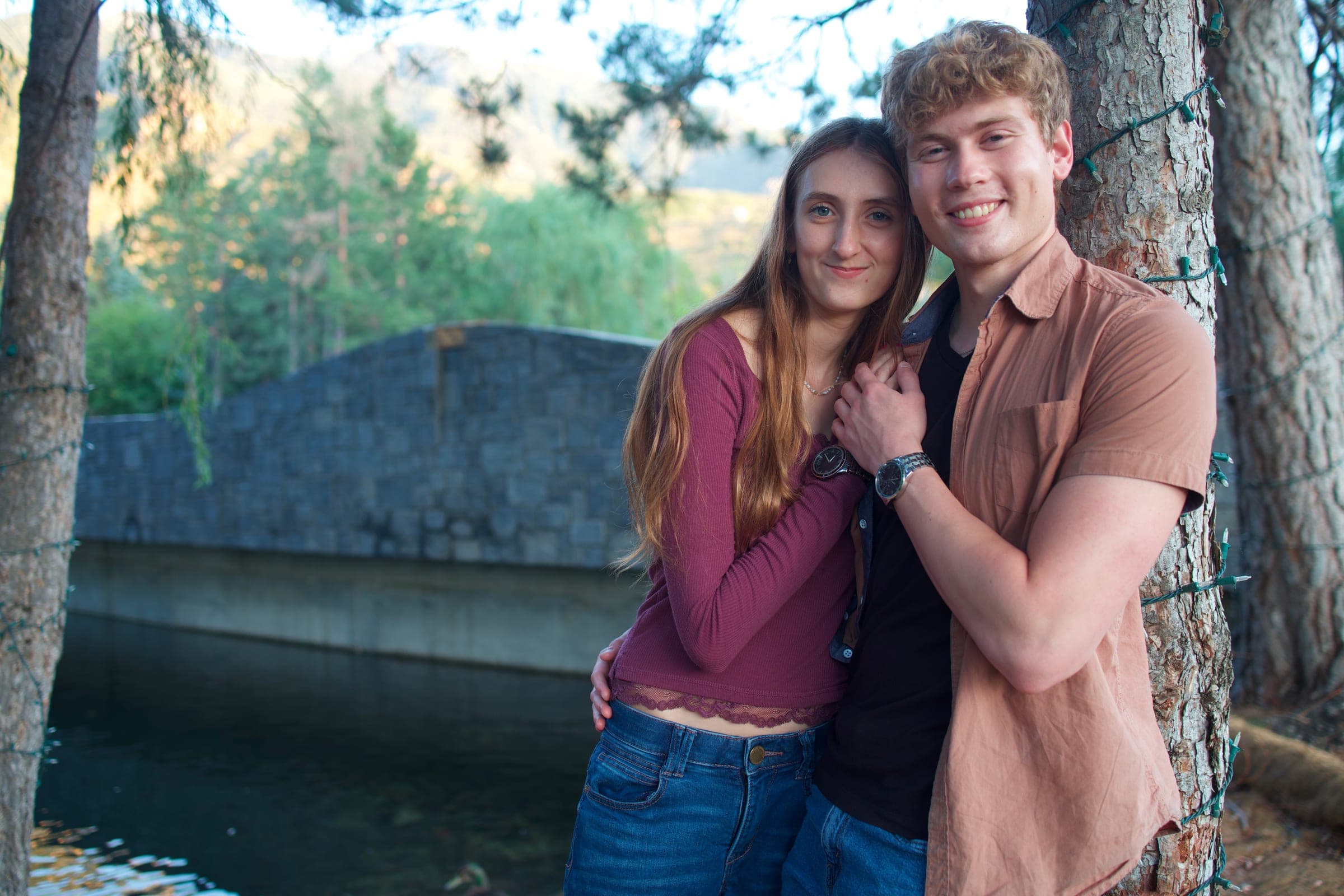 Molly and Tyler leaning on a tree by a stone bridge