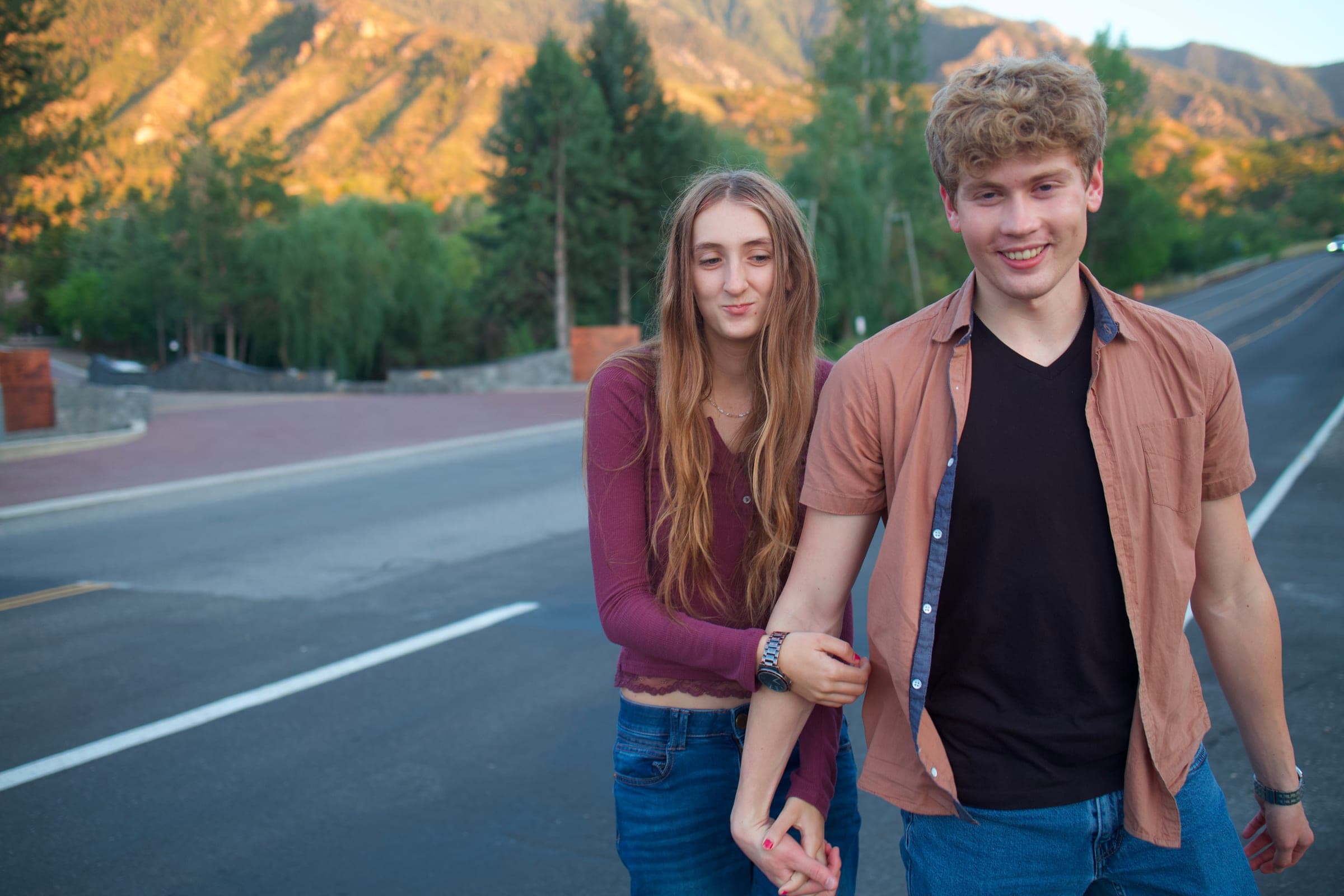 Molly and Tyler walking hand in hand along a mountain road at golden hour